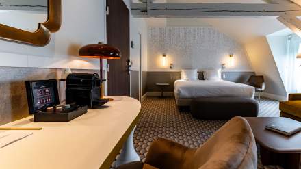 Chambre spacieuse et élégante de l’Hôtel Continental Reims, avec lit double, coin bureau équipé d’une machine à café et fauteuils confortables.