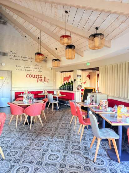 Salle lumineuse du restaurant Courtepaille avec tables dressées, banquettes rouges, chaises colorées et luminaires suspendus sous un plafond en bois clair.
