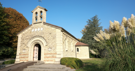 Chapelle en pierre de style roman avec clocher à deux ouvertures, entourée de verdure sous un ciel bleu, à Poligny dans le Jura – Fayet Hospitality