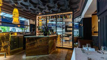 Bar élégant du Continental Reims, avec comptoir doré et étagères éclairées présentant bouteilles et verrerie dans une ambiance chaleureuse.