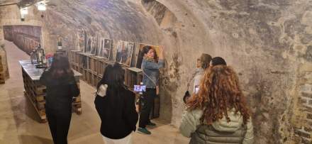 Visite guidée dans une cave voûtée avec murs en pierre, présentation de photos et bouteilles exposées – Fayet Hospitality
