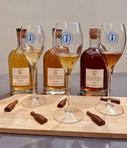 Trois verres de dégustation remplis de spiritueux disposés sur un plateau en bois avec bouteilles artisanales en arrière-plan et chocolats décoratifs - Fayet Hospitality