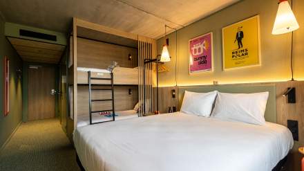 Chambre familiale du greet hôtel Reims Tinqueux avec grand lit double, lits superposés en bois, éclairage chaleureux et affiches colorées en décoration murale.
