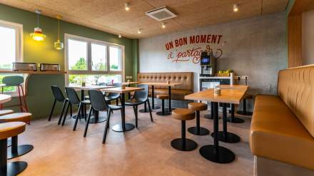 Salle de petit-déjeuner de l’Hôtel Ibis Budget Reims Thillois, avec banquettes confortables, tables en bois, chaises noires et message mural “Un bon moment à partager”