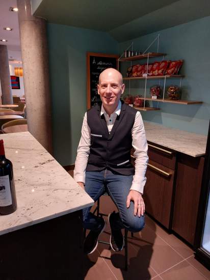 Personnel d’accueil en tenue professionnelle derrière un comptoir élégant, décor moderne avec étagères et produits exposés, hôtel à Poligny dans le Jura – Fayet Hospitality