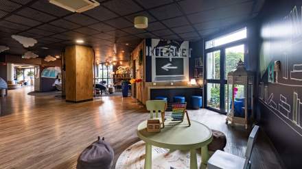 Espace famille de l’Hôtel Ibis Budget Pontault-Combault, avec coin jeux pour enfants, tables et chaises colorées, poufs, et zone de détente lumineuse décorée de motifs ludiques.
