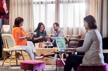Groupe de personnes échangeant dans un espace de travail convivial, avec fauteuils colorés et ambiance lumineuse.