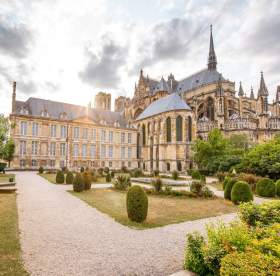 Jardin paysager devant la cathédrale Notre-Dame de Reims, monument gothique emblématique éclairé par une lumière de fin de journée.<br />