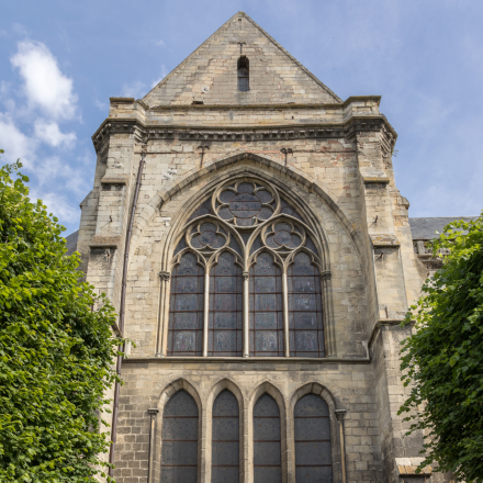 Façade en pierre d’une église gothique avec grande fenêtre à vitraux et détails architecturaux sous ciel bleu - Fayet Hospitality