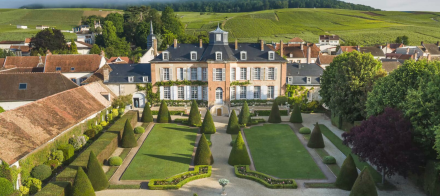 Vue aérienne d’un domaine viticole avec bâtiment historique en briques, jardins symétriques et vignobles verdoyants à l’arrière-plan – Fayet Hospitality