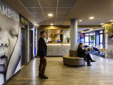 Hall d’accueil moderne avec comptoir de réception, espace lounge et décoration contemporaine, sol en bois clair et éclairage chaleureux, hôtel à Poligny dans le Jura – Fayet Hospitality
