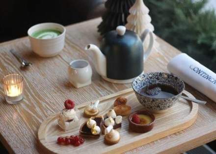 Plateau gourmand avec mignardises sucrées, théière noire, tasse de thé et bougie sur une table en bois élégante – Fayet Hospitality