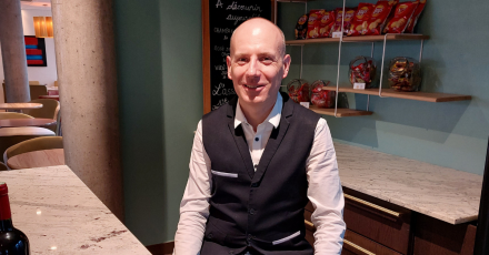 Comptoir élégant en marbre avec bouteille de vin, étagères garnies de produits et ardoise décorative en arrière-plan, espace convivial dans un hôtel – Fayet Hospitality