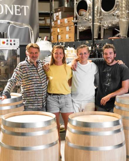 Quatre personnes posant dans une cave avec plusieurs tonneaux en bois et cuves en inox en arrière-plan – Fayet Hospitality