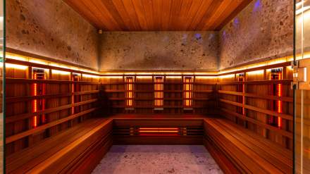 Sauna moderne de l’Hôtel Continental Reims, avec bancs en bois, éclairage chaleureux et parois en pierre naturelle.