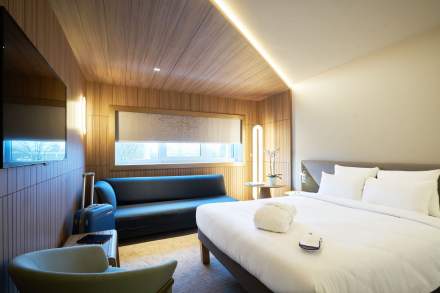 Chambre moderne et lumineuse du Novotel Collégien Marne-la-Vallée, avec grand lit double, canapé bleu, mobilier en bois et ambiance chaleureuse.