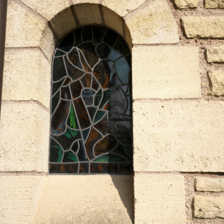 Vitrail coloré à motifs abstraits intégré dans une fenêtre en pierre de style roman, détail architectural de la chapelle à Poligny dans le Jura – Fayet Hospitality