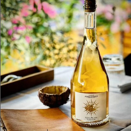 Bouteille de champagne Joseph Desruets posée sur une table élégante avec décor floral en arrière-plan - Fayet Hospitality
