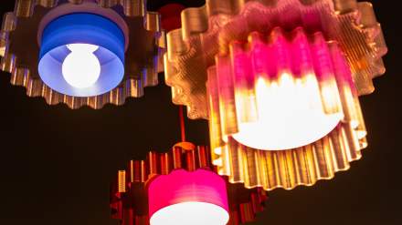 Suspensions colorées aux formes ondulées éclairées dans l’espace commun de l’Hôtel Ibis Budget Reims Thillois.