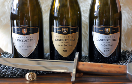 Trois bouteilles de champagne Lancelot-Piana millésime 2014 avec une épée décorative et une bague posées devant – Fayet Hospitality