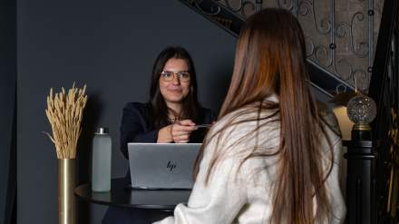 Scène à la réception de l’Hôtel Continental : une employée remet la carte de chambre à une cliente devant un bureau équipé d’un ordinateur.