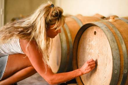 Personne inspectant un grand tonneau en bois dans une cave à vin, lumière chaude et ambiance authentique, Fayet Hospitality.