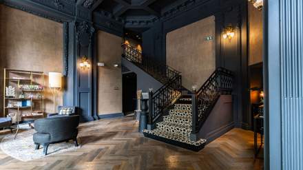 Hall d’entrée élégant de l’Hôtel Continental Reims, avec escalier ornementé, parquet en chevron et espace lounge décoré de meubles modernes.