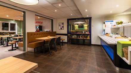 Salle de petit-déjeuner de l’Hôtel Ibis Budget Reims Thillois, avec buffet varié, banquettes confortables, tables modernes et espace lumineux.