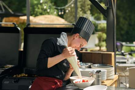 Cheffe préparant un dessert en plein air au Novotel Collégien Marne-la-Vallée, ajoutant une crème à la poche à douille sur un bowl de fruits.