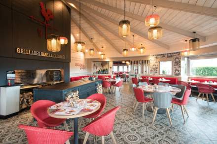 Grande salle du restaurant Courtepaille, avec cheminée ouverte pour grillades, tables dressées, chaises colorées et luminaires suspendus.