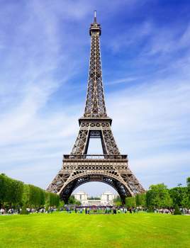 Vue de la tour Eiffel à Paris depuis le Champ-de-Mars, sous un ciel bleu légèrement nuageux.
