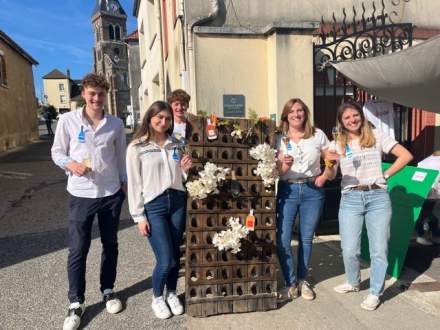 Groupe de personnes debout en extérieur devant un bâtiment historique avec présentoir de bouteilles décoré de fleurs, ambiance conviviale et festive - Fayet Hospitality