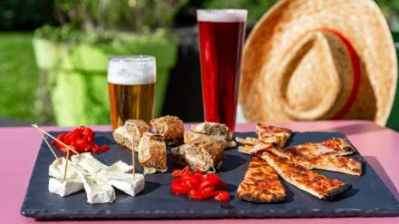 Plateau apéritif de l’Hôtel Ibis Budget Pontault-Combault, composé de fromages, bouchées salées, parts de pizza et poivrons marinés, accompagné de bières servies en extérieur.