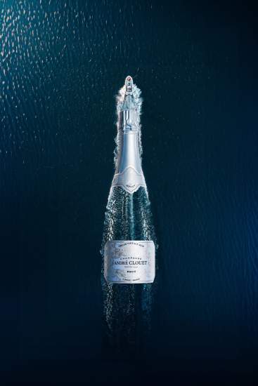 Bouteille de champagne André Clouet vue du dessus flottant sur une surface d’eau sombre, composition élégante et créative - Fayet Hospitality