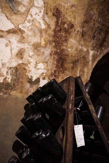 Support en bois incliné avec bouteilles de vin stockées tête en bas dans une cave voûtée aux murs patinés – Fayet Hospitality