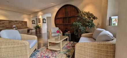 Salon chaleureux avec fauteuils en rotin, table basse et grande porte en bois arrondie – Fayet Hospitality