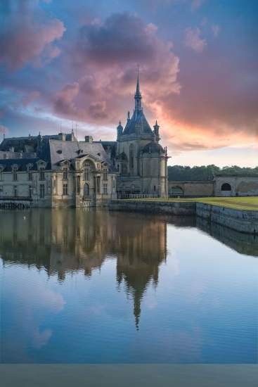 Château historique de Seine-et-Marne se reflétant dans un étang au coucher du soleil, sous un ciel aux teintes rosées.