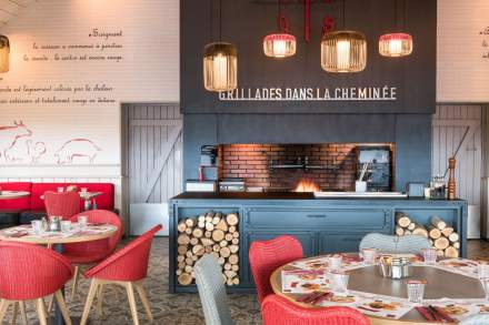 Espace grillades du restaurant Courtepaille, avec grande cheminée en briques, bois stocké, tables dressées et décor mural chaleureux.