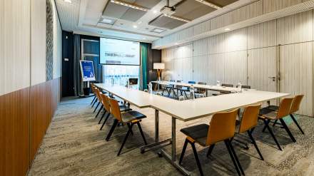 Salle de réunion moderne en configuration en U, équipée d’un vidéoprojecteur, de chaises contemporaines et de lumière naturelle.