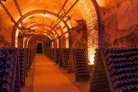 Caves champenoises voûtées éclairées d’une lumière chaude, avec rangées de bouteilles de champagne sur pupitres.