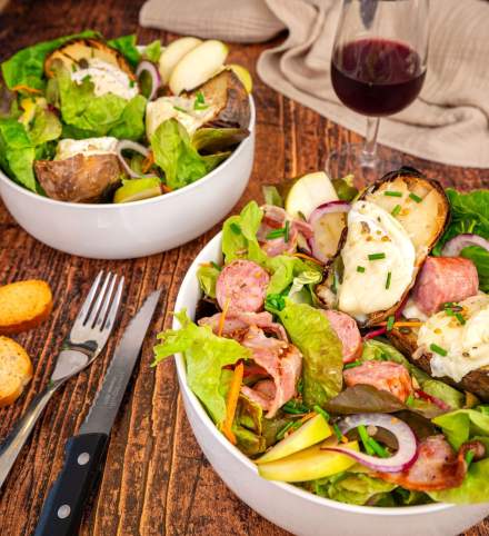 Bol de salade gourmande du restaurant Courtepaille, composée de saucisses, légumes frais, pommes, oignons rouges et pommes de terre gratinées au fromage, accompagné d’un verre de vin rouge.