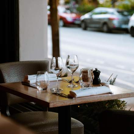 Table élégamment dressée avec verres à vin, couverts et serviettes blanches dans un restaurant avec vue sur la rue – Fayet Hospitality