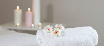 Serviettes blanches roulées avec fleurs décoratives et bougies allumées en arrière-plan, ambiance spa relaxante – Fayet Hospitality