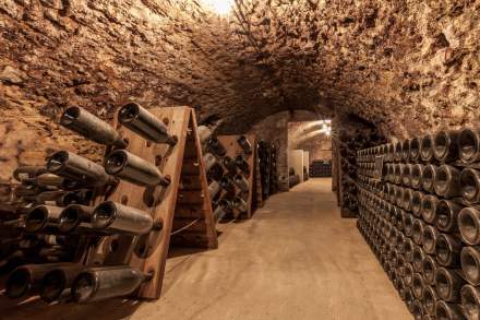 Cave voûtée traditionnelle avec murs en pierre, rangées de bouteilles de vin stockées sur pupitres en bois – Fayet Hospitality