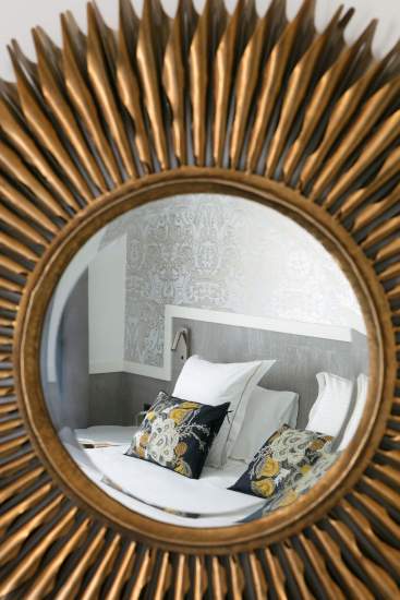 Reflet d’un lit avec coussins décoratifs dans un miroir rond à cadre doré, décoration élégante et raffinée - Fayet Hospitality