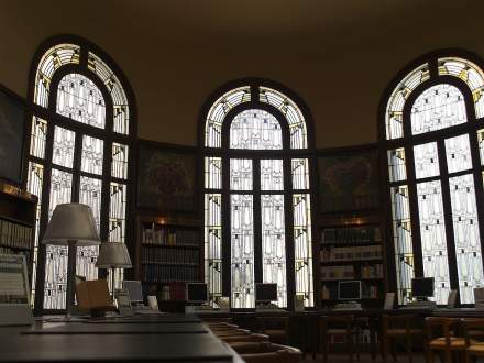 Salle de lecture avec grandes fenêtres en arc ornées de vitraux, lampes de bureau et rangées de livres et ordinateurs – Fayet Hospitality