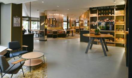 Hall d’accueil moderne du Novotel Collégien Marne-la-Vallée, avec espace lounge, table d’accueil et comptoir local proposant des produits régionaux.