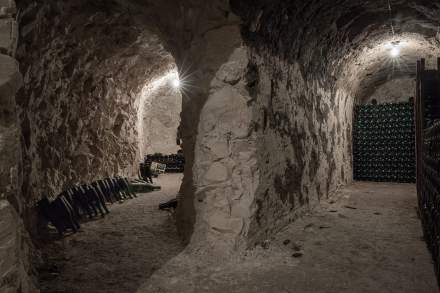 Cave voûtée en pierre avec rangées de bouteilles de vin empilées et sol en terre battue, ambiance authentique et traditionnelle - Fayet Hospitality