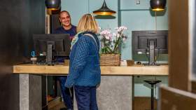 Employé à l’accueil échangeant avec une cliente devant un comptoir moderne décoré de fleurs.<br />