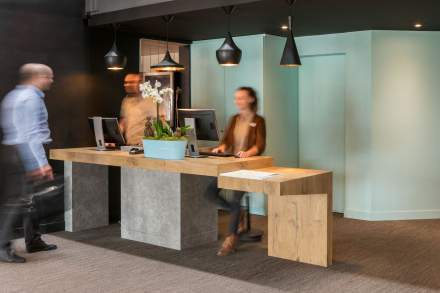 Comptoir de réception moderne avec deux personnes accueillant les clients dans un espace lumineux et contemporain.